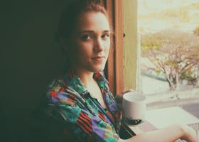 A serene portrait of a woman enjoying coffee by a window in a colorful shirt.