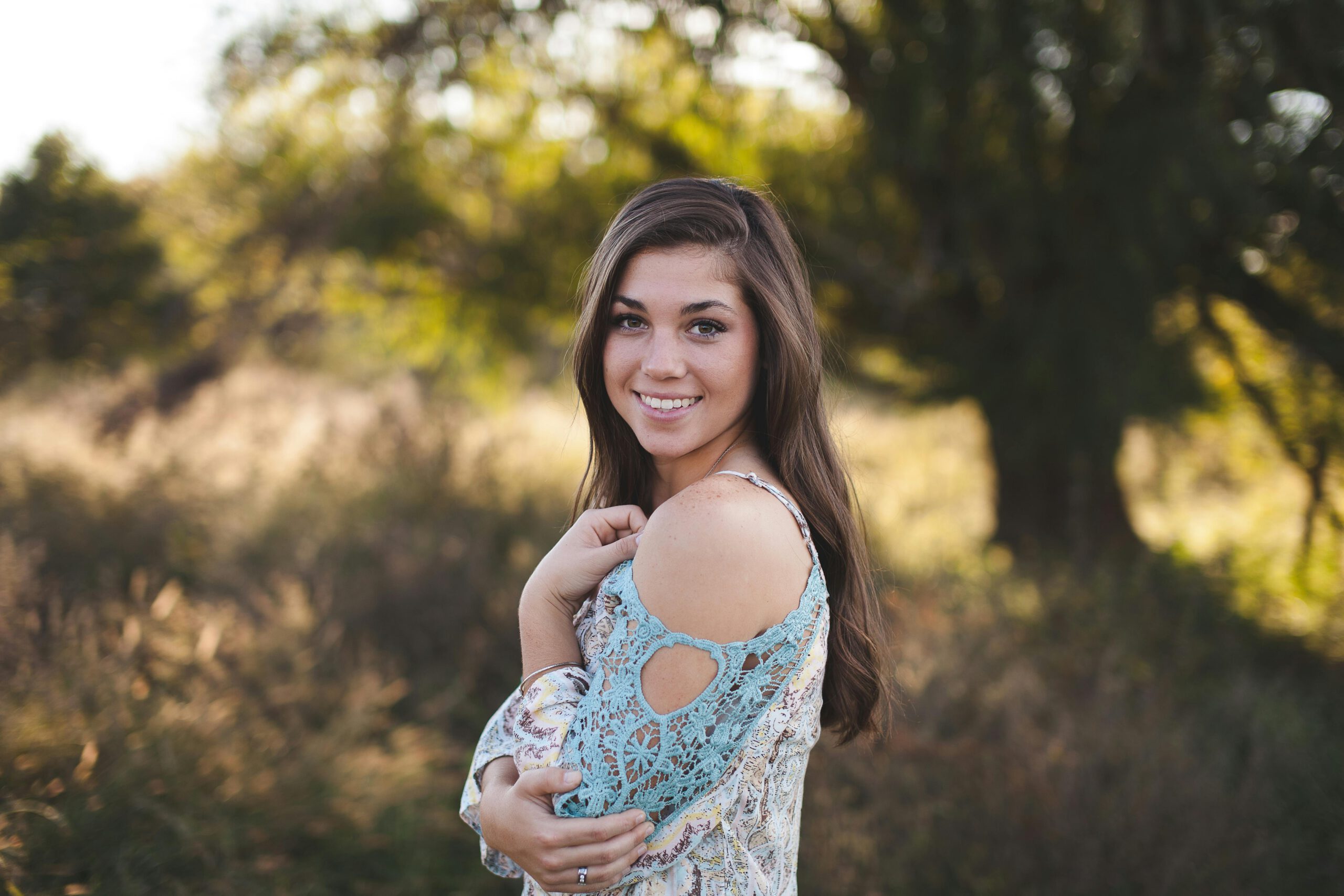 A young woman joyfully smiling in a summer dress, surrounded by nature.